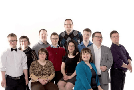 Farklı yaş gruplarından Down sendromlu bireylerin birlikte yer aldığı, kameraya bakarak poz verdikleri grup fotoğrafı.